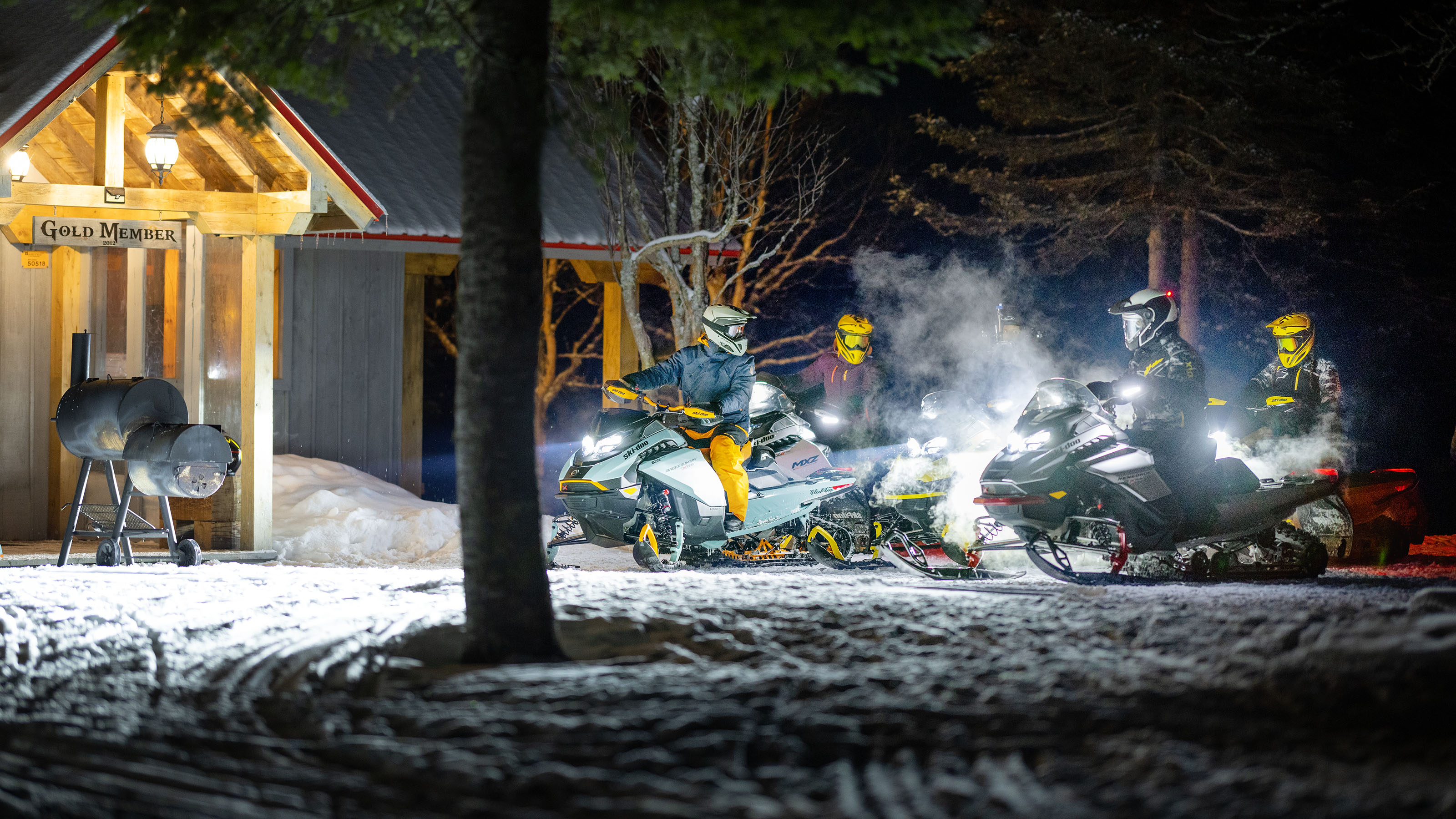 En gruppe snøscooterkjørere har stoppet foran en hytte i mørket
