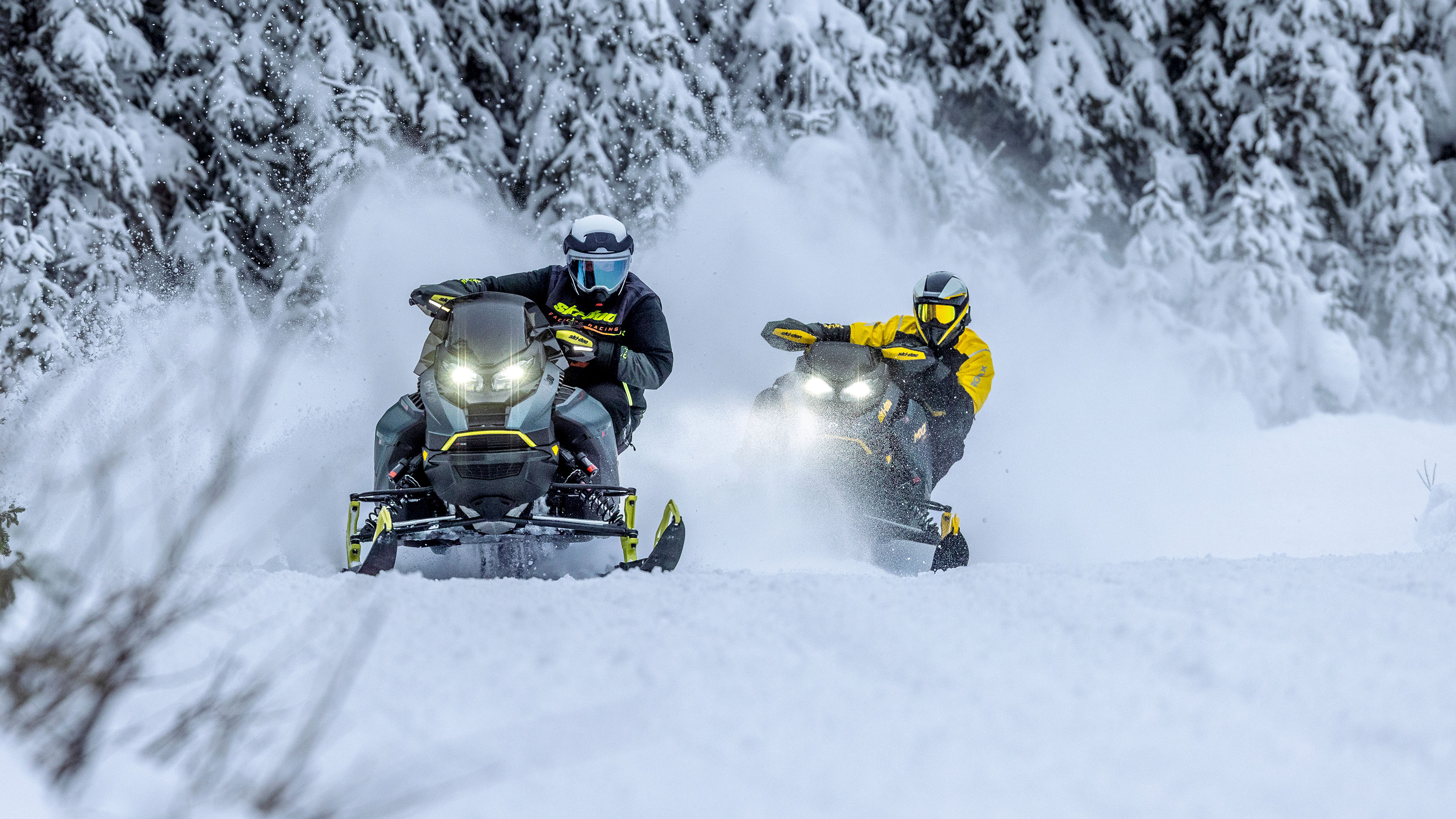 Två Ski-Doo-snöskotrar kör i hög fart på en snöig led