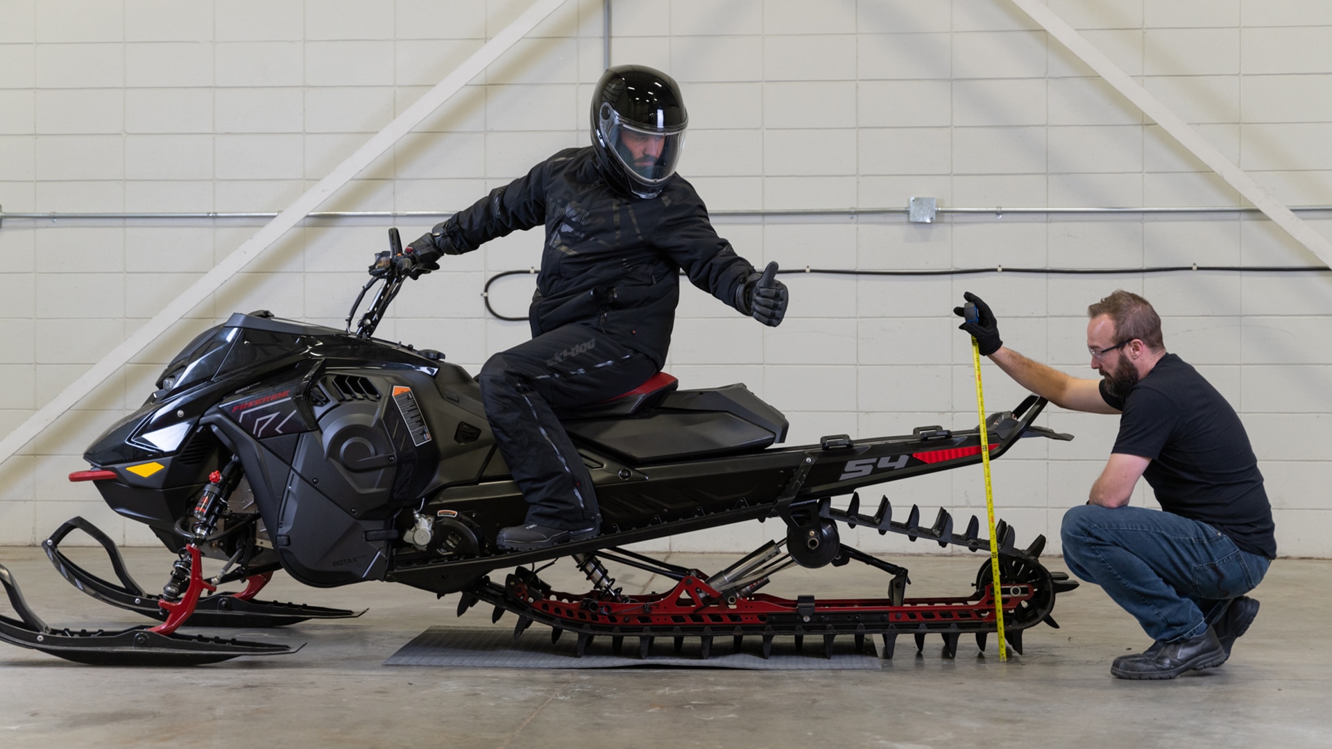 Ski-Doo rider on vehicle doing a thumbs up, while his friend measures the height of the rear bumper
