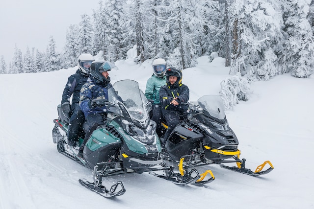 Two Ski-Doo snowmobiles idle while the riders are talking