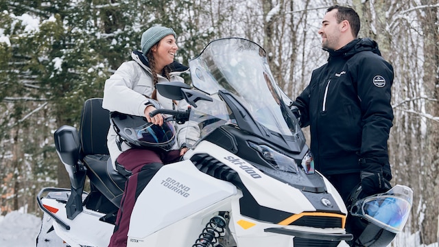 Woman sitting on a Ski-Doo Grand Touring electric snowmobile while talking to a fellow rider