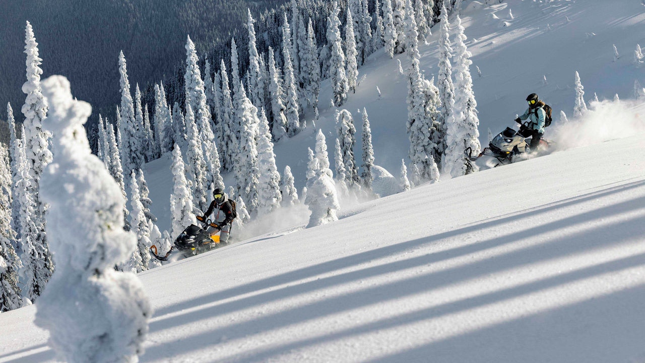 Two people riding Ski-Doo Summit snowmobiles in a mountain