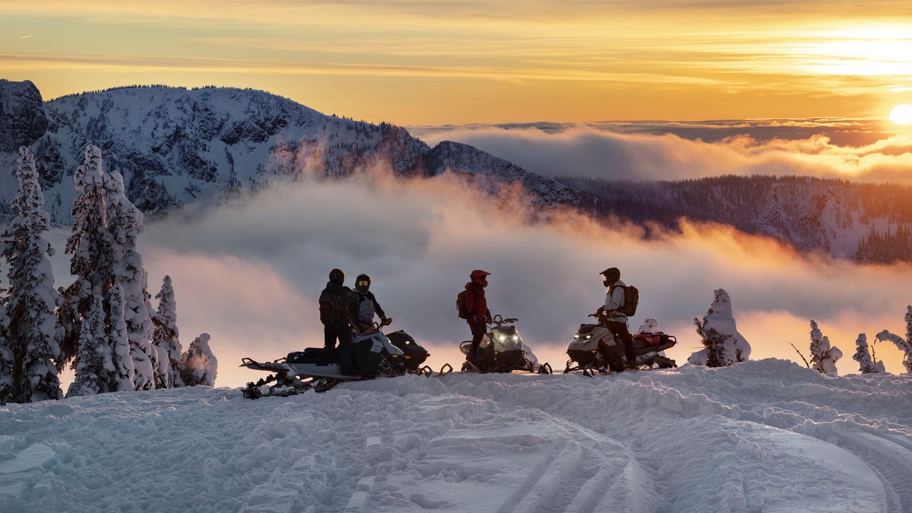 Groupe de motoneigistes Ski-Doo au sommet d'une montagne au coucher de soleil