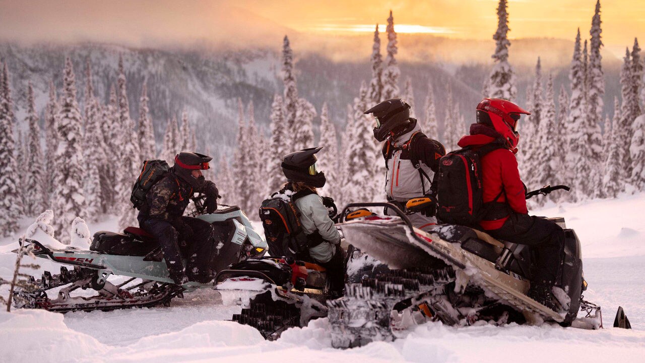 Group of riders on their sleds at the top of a mountain at sunset 