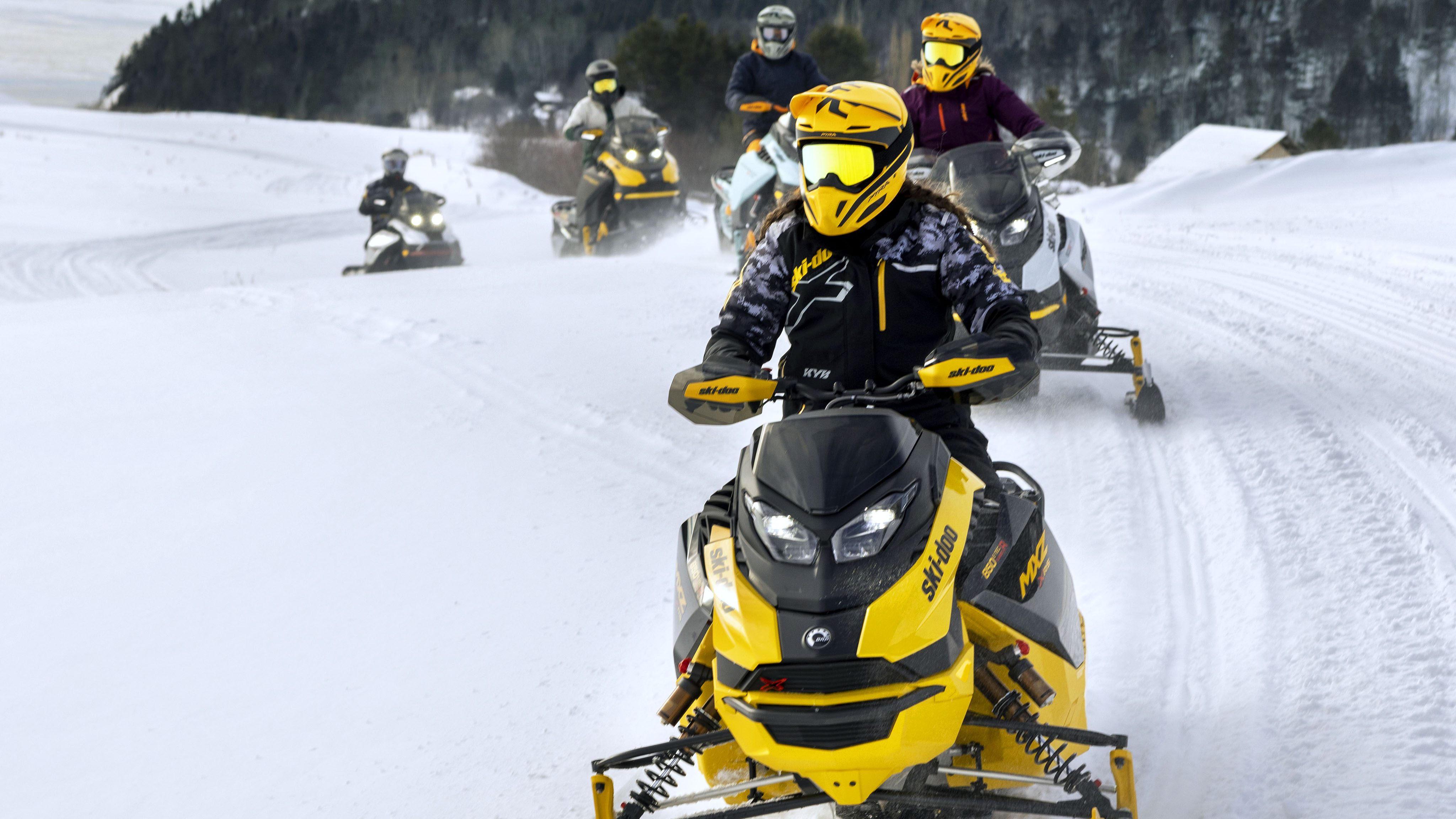 Cinq motoneigistes conduisant des Ski-Doo en sentier