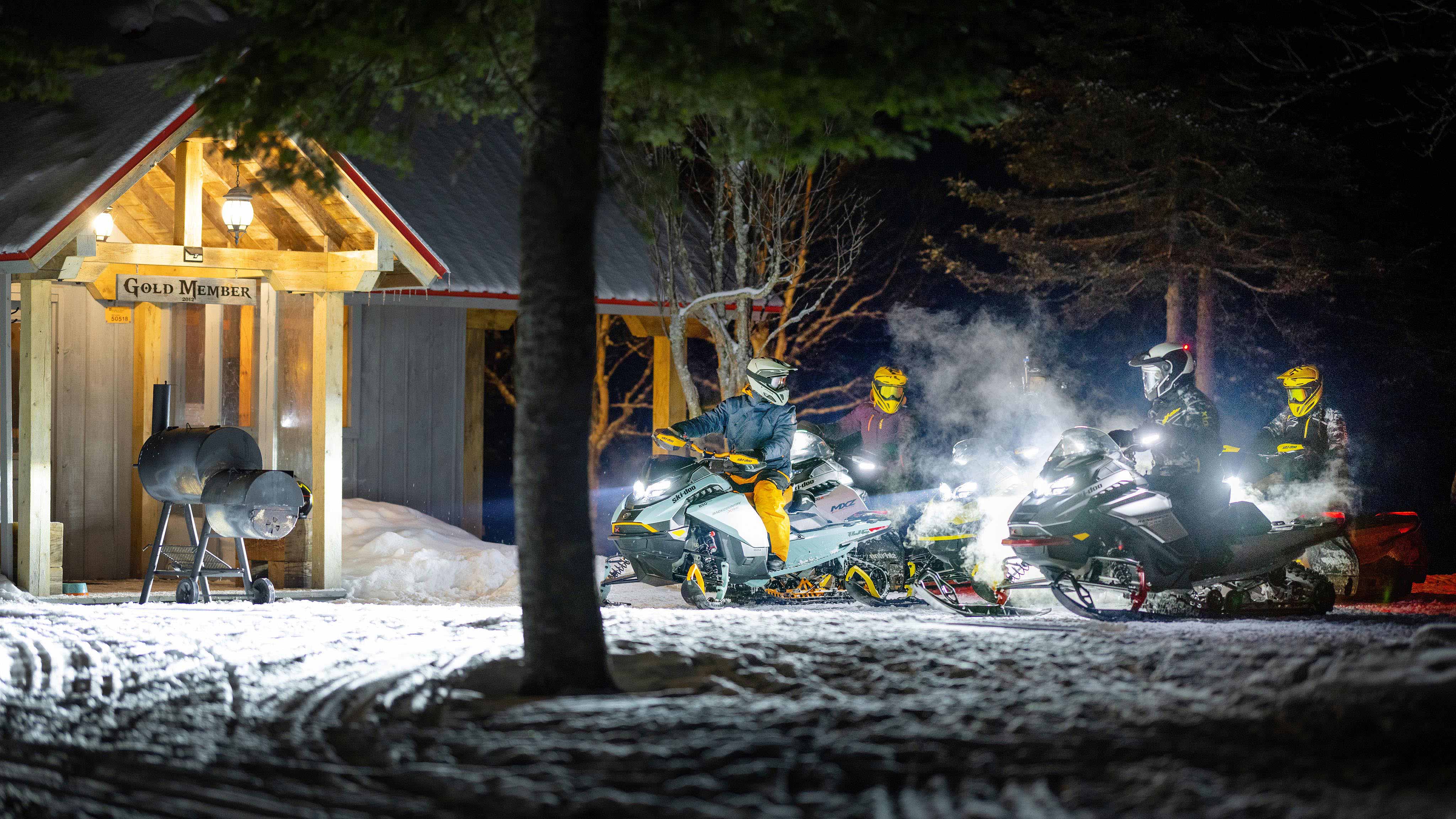 Group of snowmobilers next to a cottage at night on their Ski-Doo