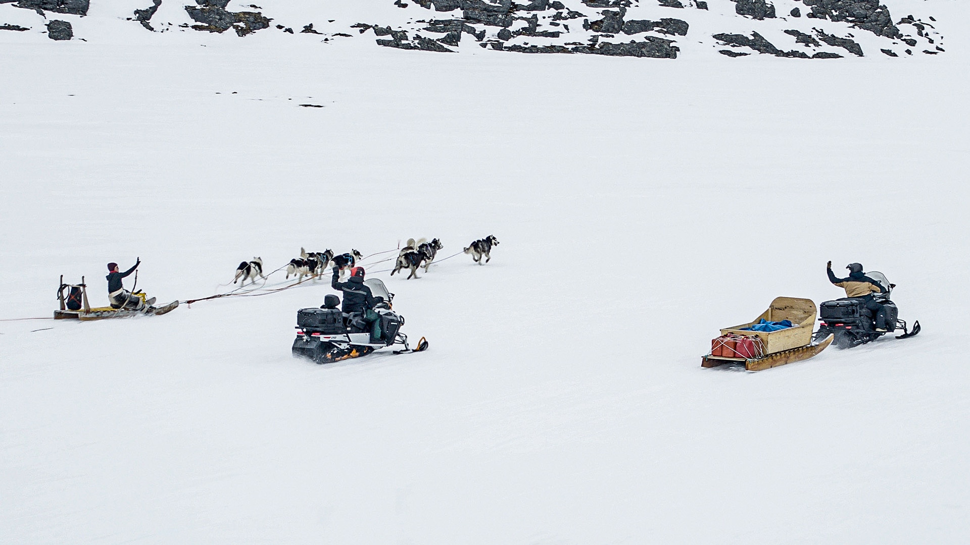 Deux hommes conduisant des motoneiges Ski-Doo et passant à côté d'un traîneau à chien