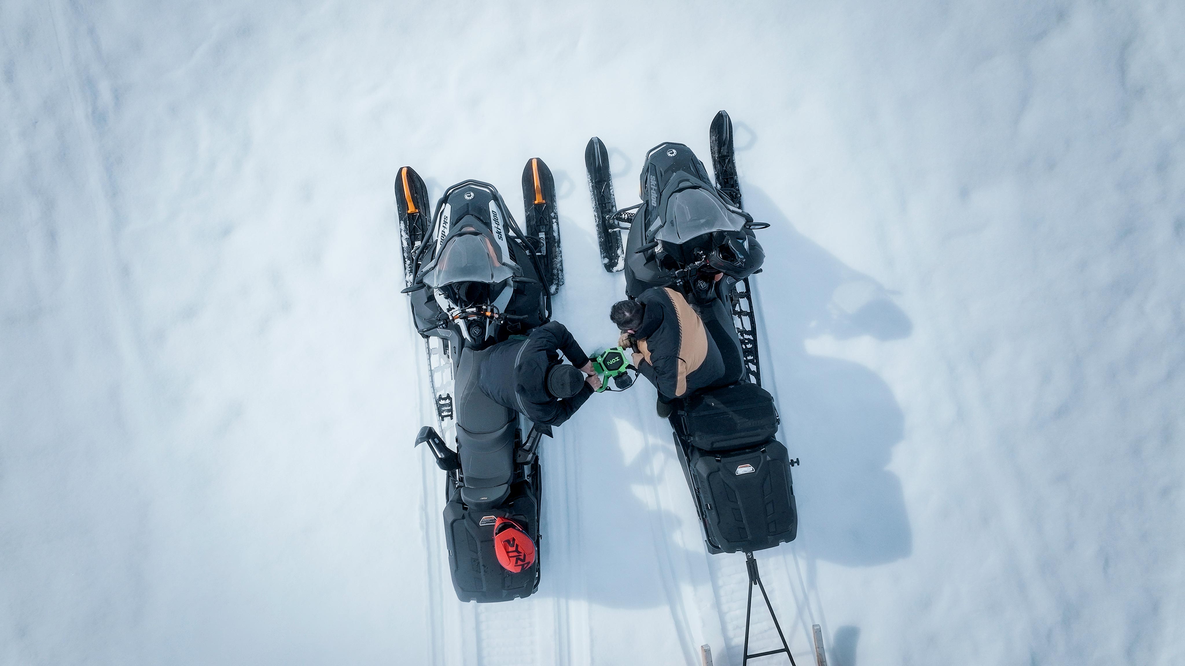 Två män på sina Ski-Doo snöskotrar gör ett hål i isen