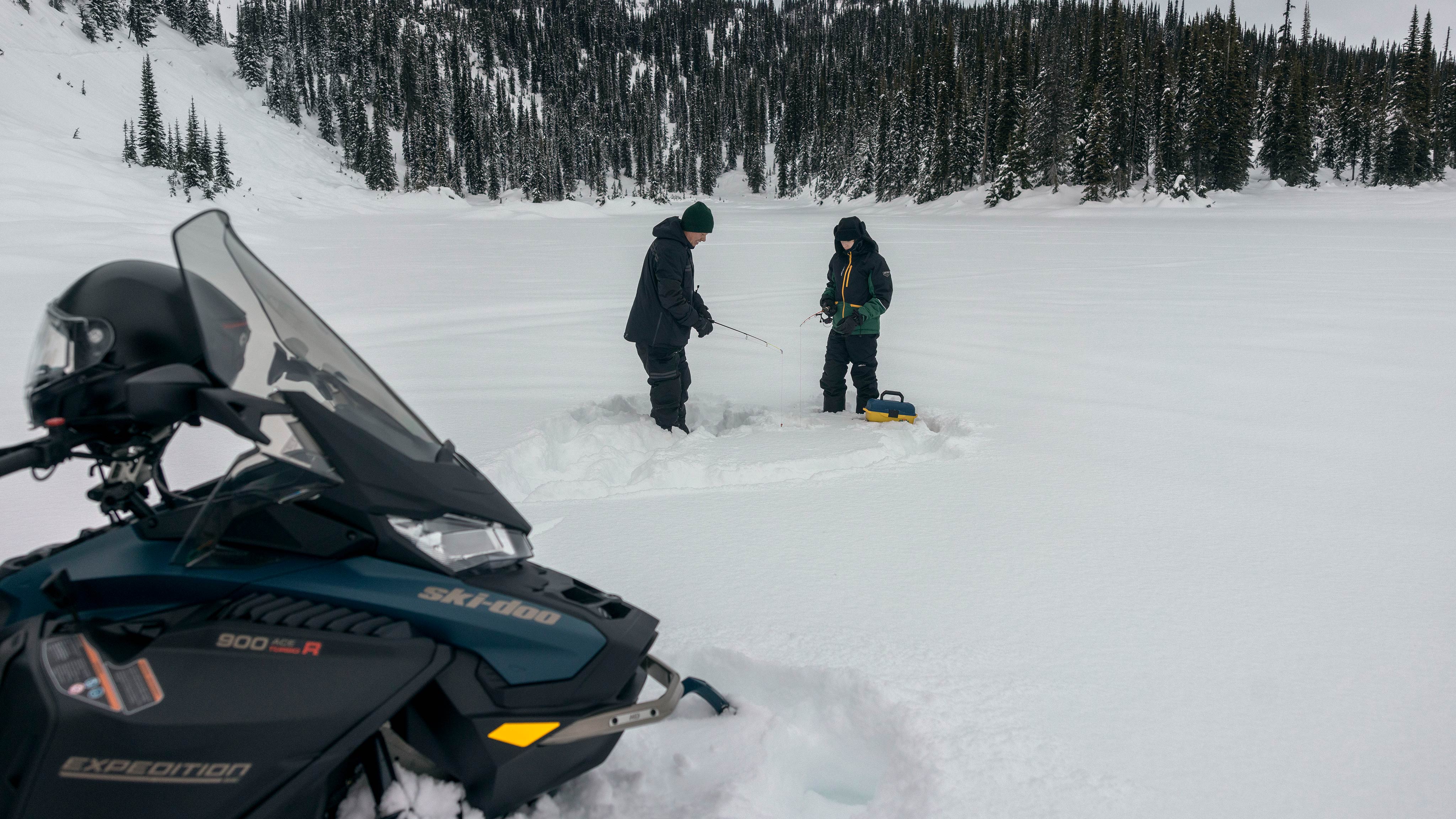 Two snowmobile riders fishing next to a Ski-Doo Crossover Expedition