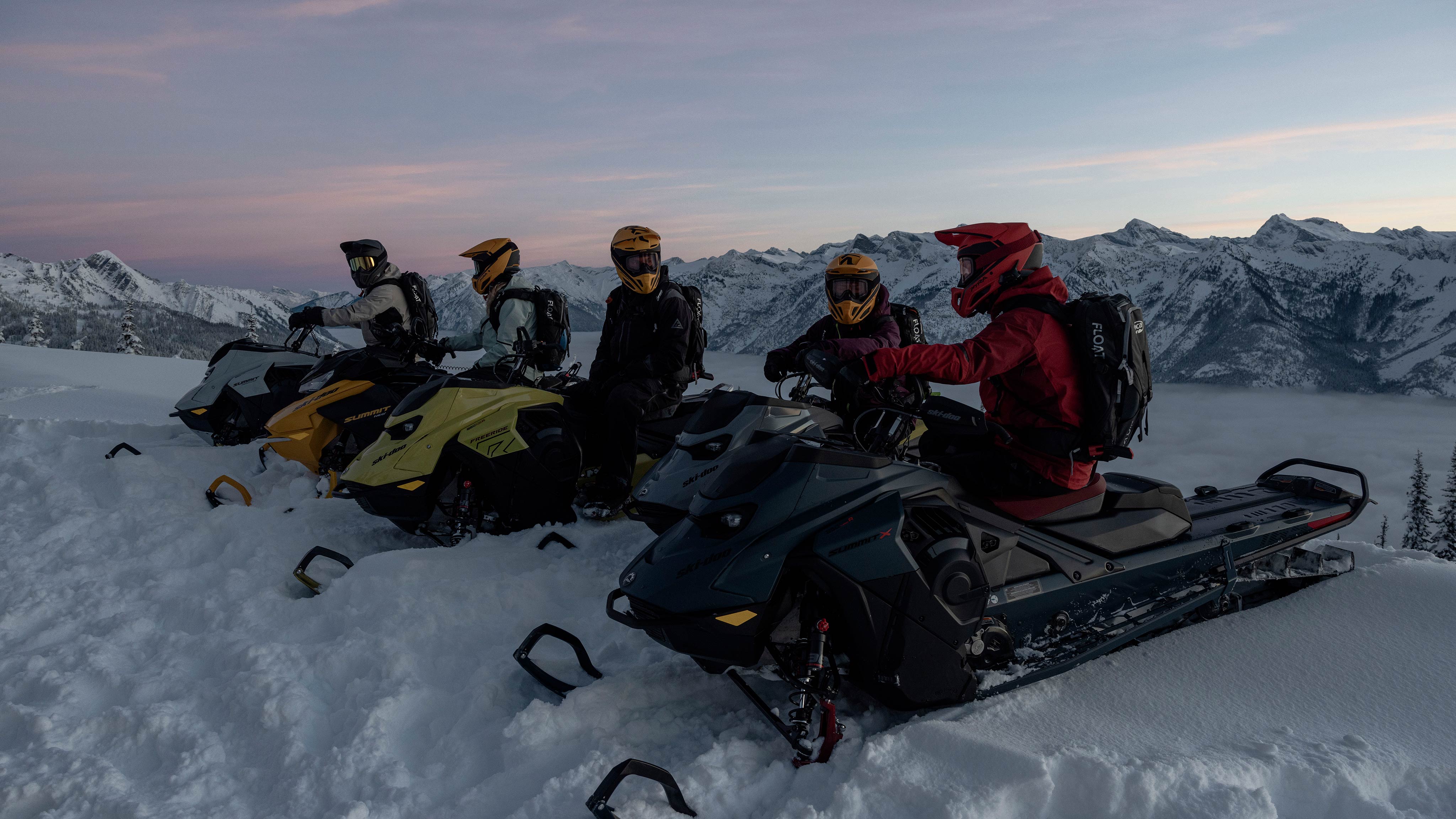 Five snowmobile riders on top of a snowy mountain