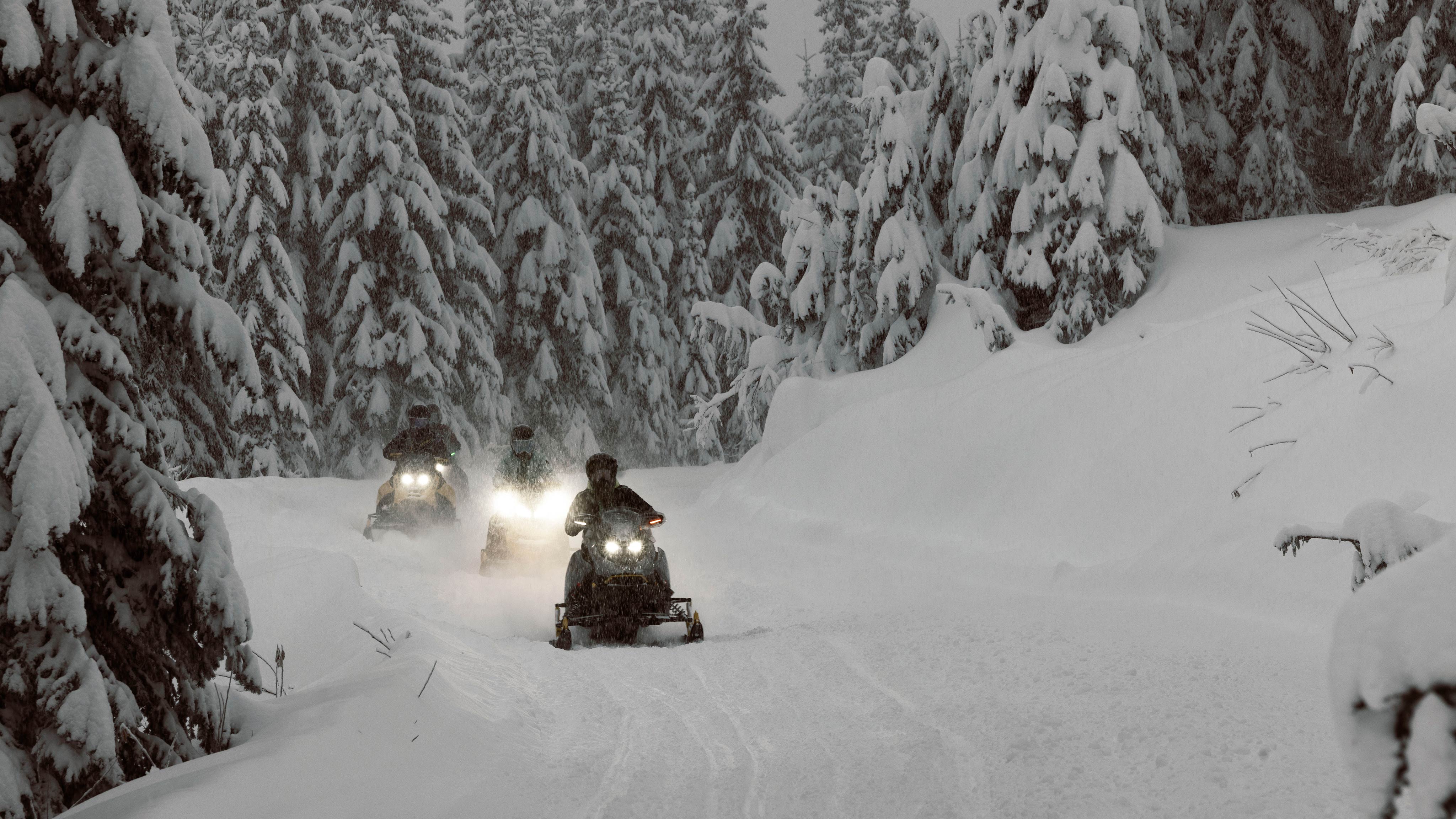 Three riders taking a break from a snowy ride on their Ski-Doo snowmobiles