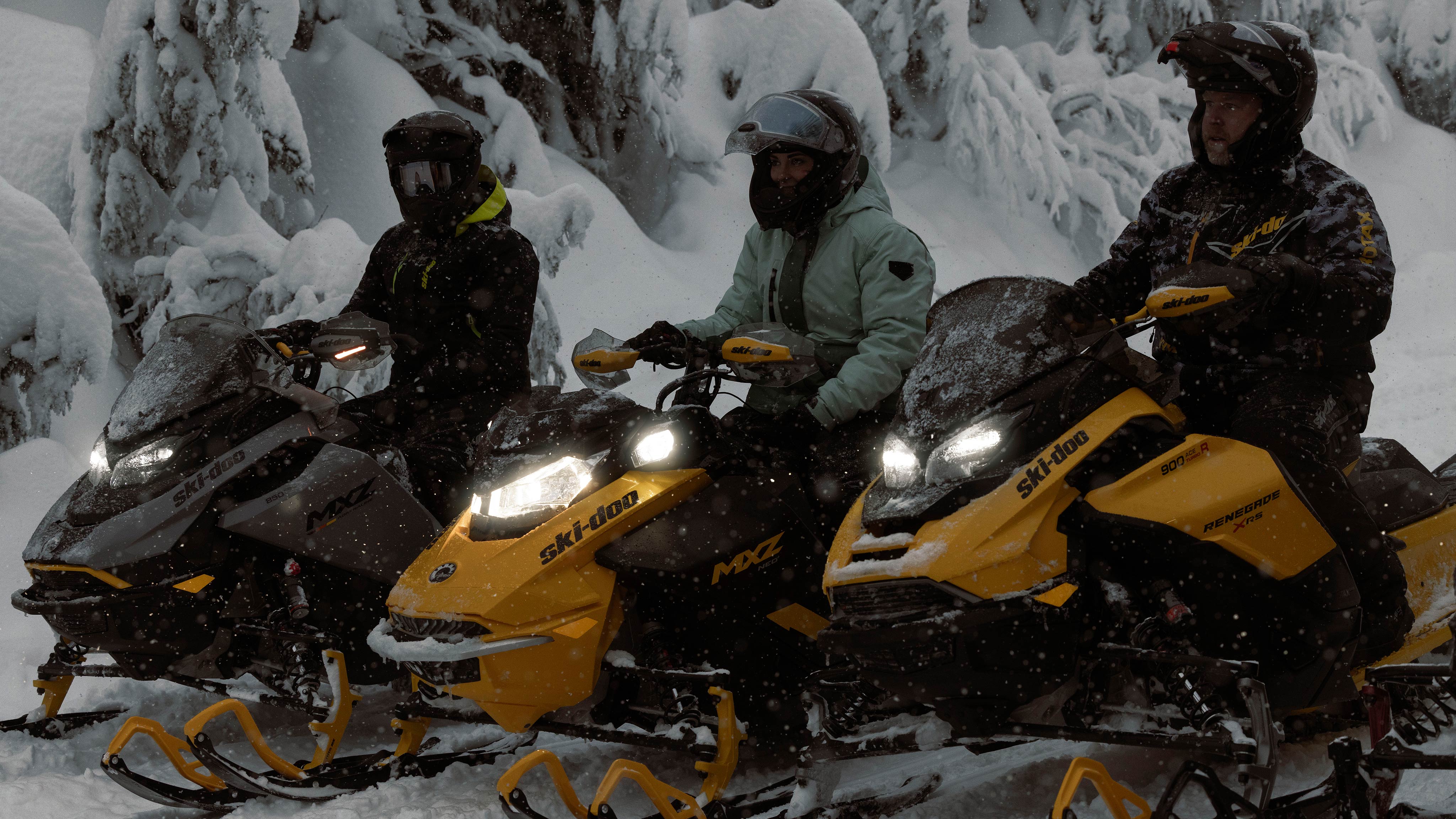 Trois motoneigistes prenant une pause de leur randonnée enneigée sur leur Ski-Doo