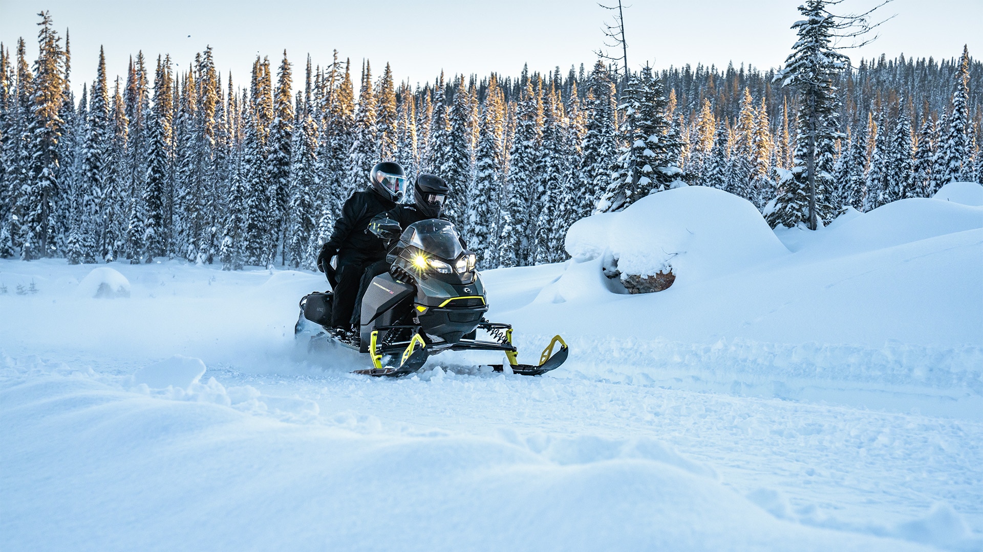 Two people riding a Backcountry snowmobile on a snowy trail