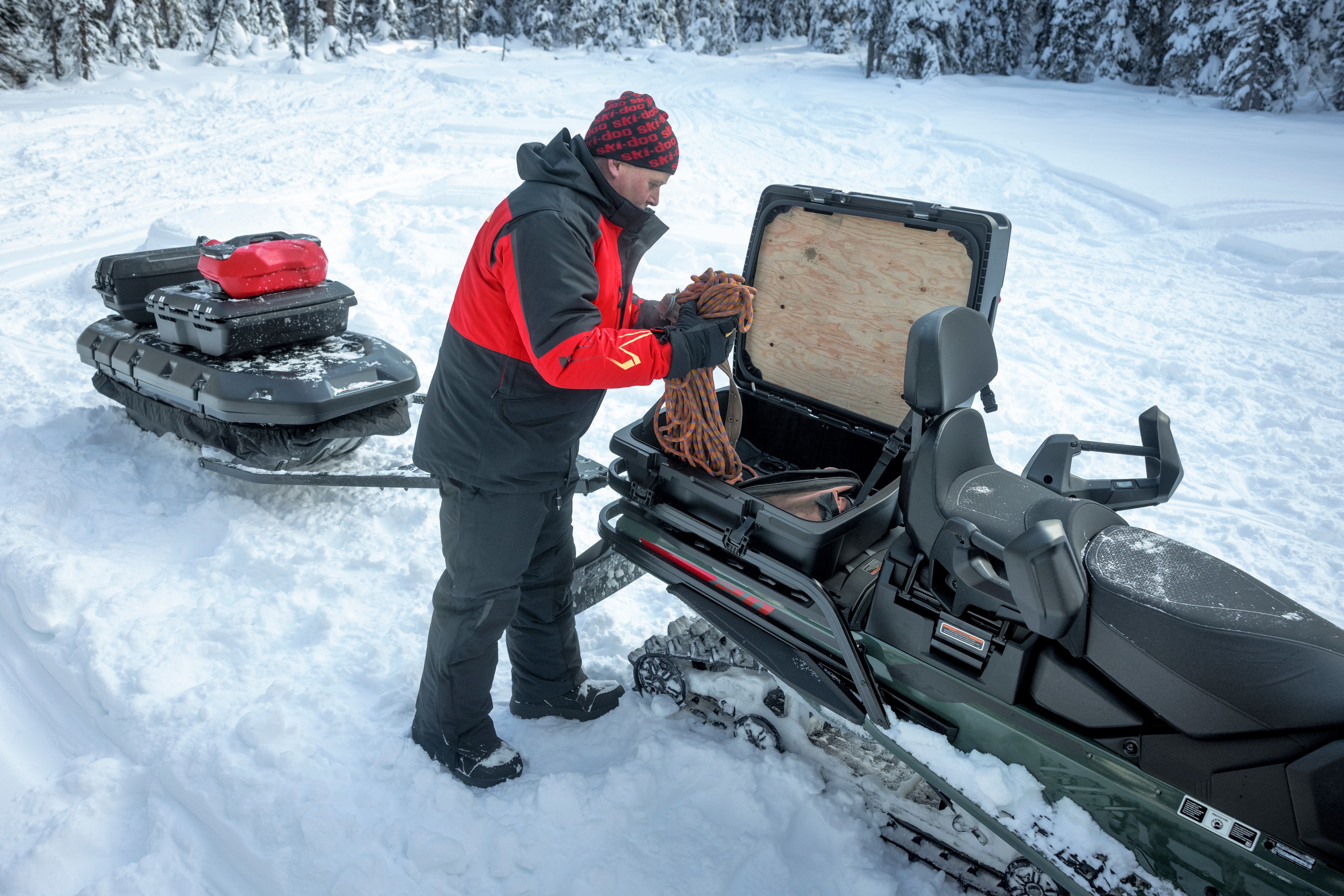 Snowmobiler using the storage box on his 2026 Ski-Doo Expedition snowmobile in a snowy forest.