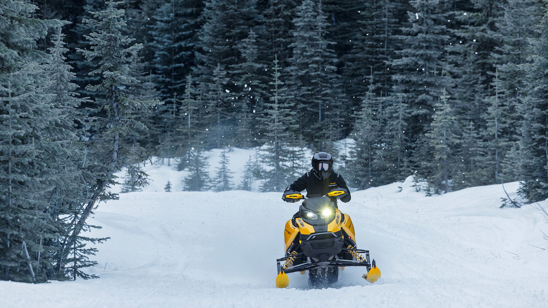 Rider riding a 2027 Ski-Doo Backcountry snowmobile on a snowy field surrounded by trees