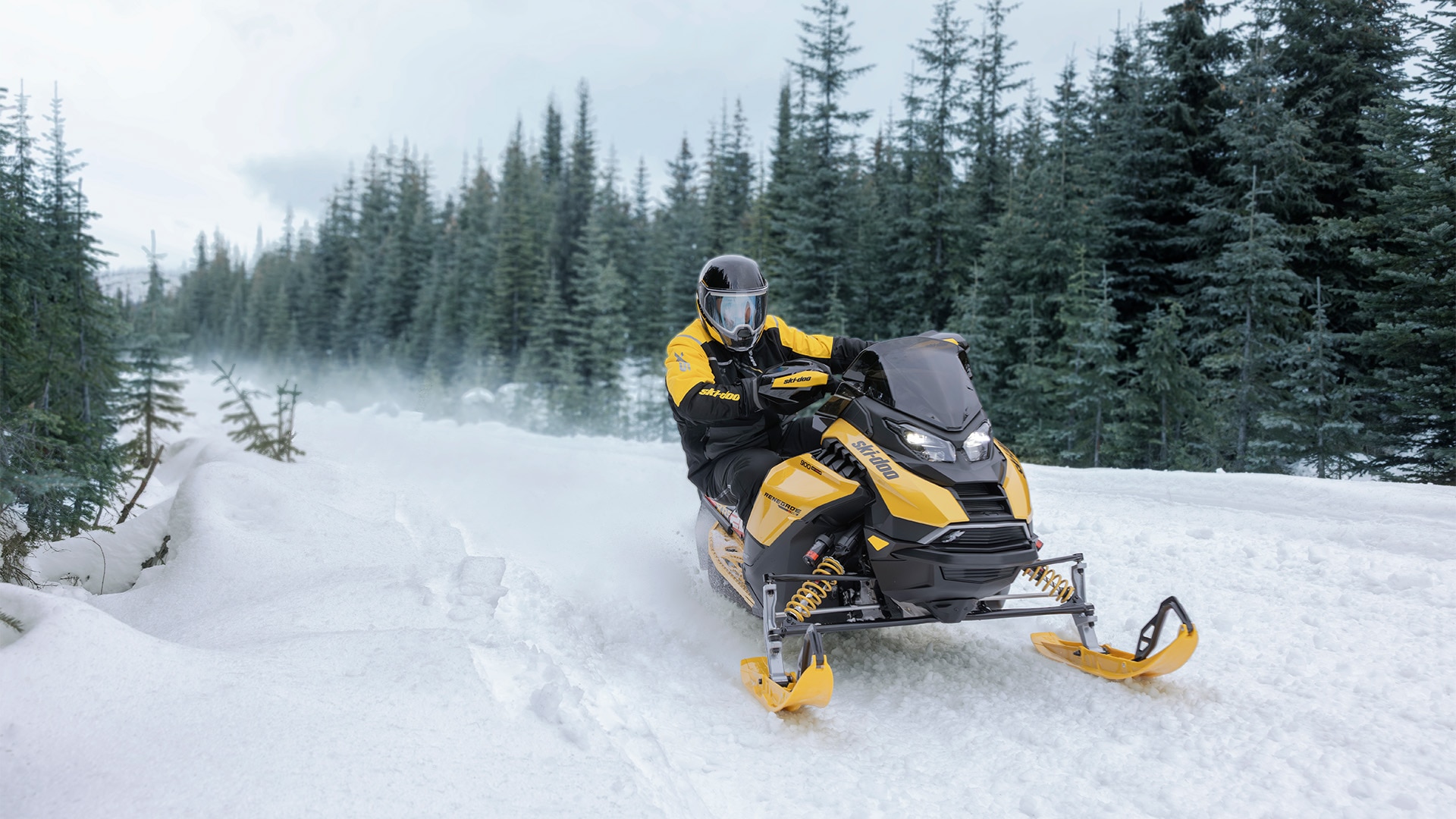 Rider riding a 2027 Ski-Doo Renegade X-RS snowmobile on a snowy field surrounded by trees