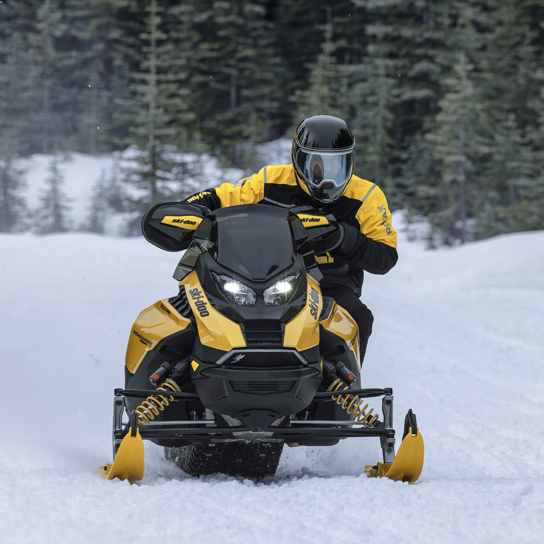 Three Ski-Doo snowmobiles riding on a groomed trail in the middle of a forest