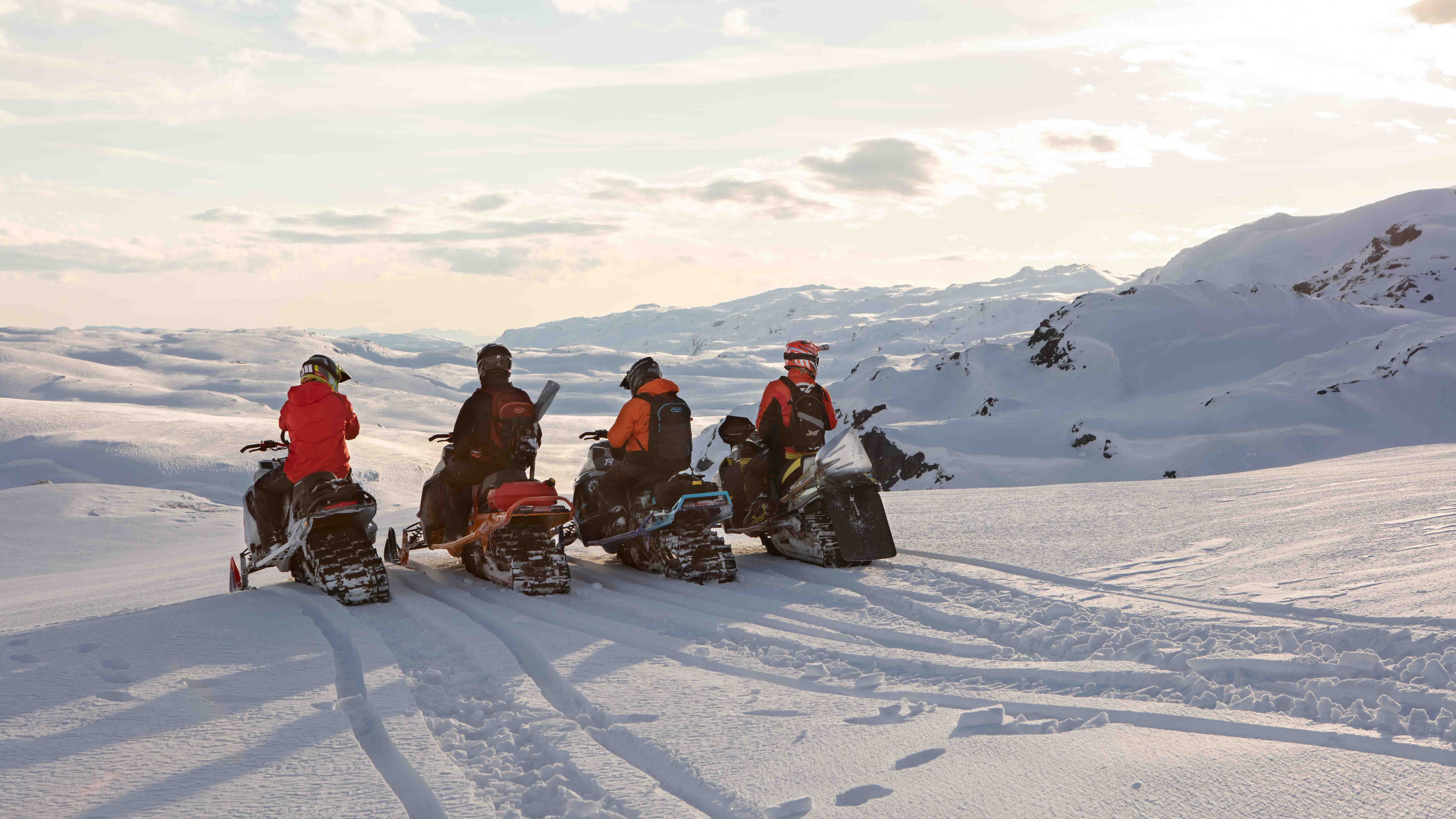 Ski-Doo snowmobiles parked in mountains with riders