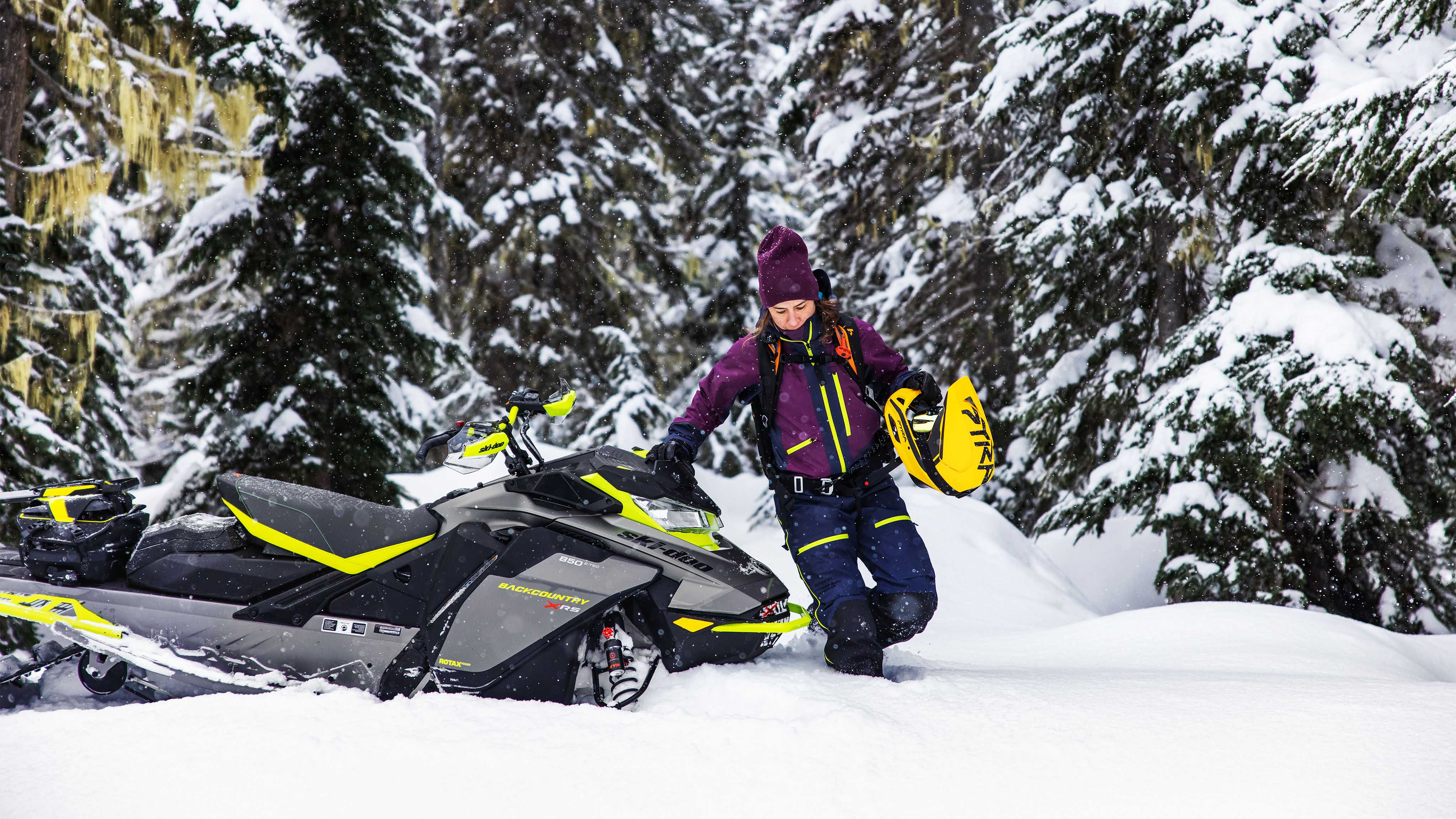 Woman walking in snow next to her ski-Doo Backcountry X-RS