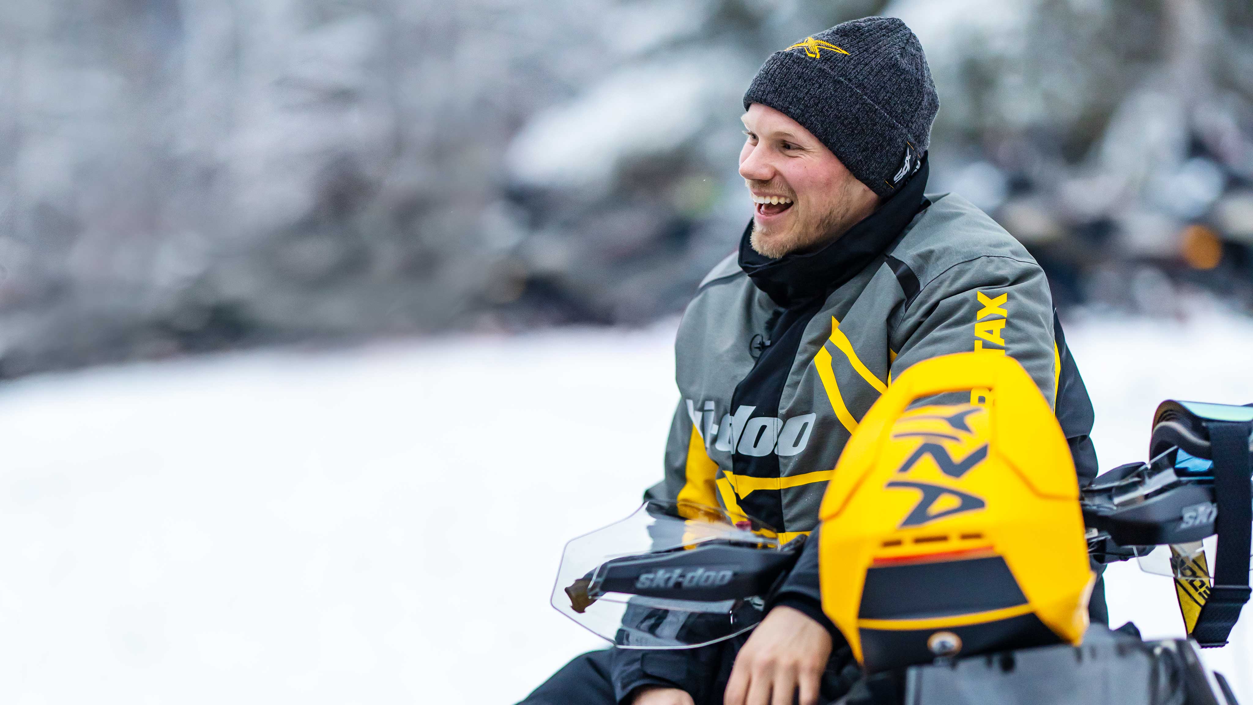 Homme assis sur sa motoneige Ski-Doo et portant le manteau X-Team