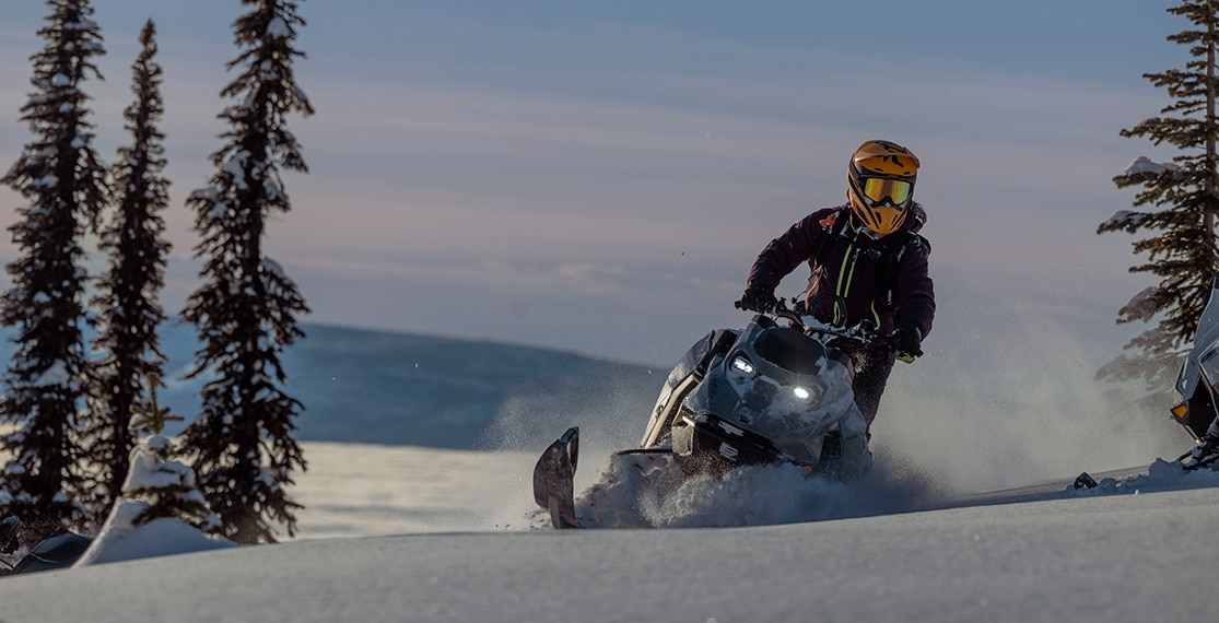 A man riding his 2025 Ski-Doo Summit snowmobile through the mountains