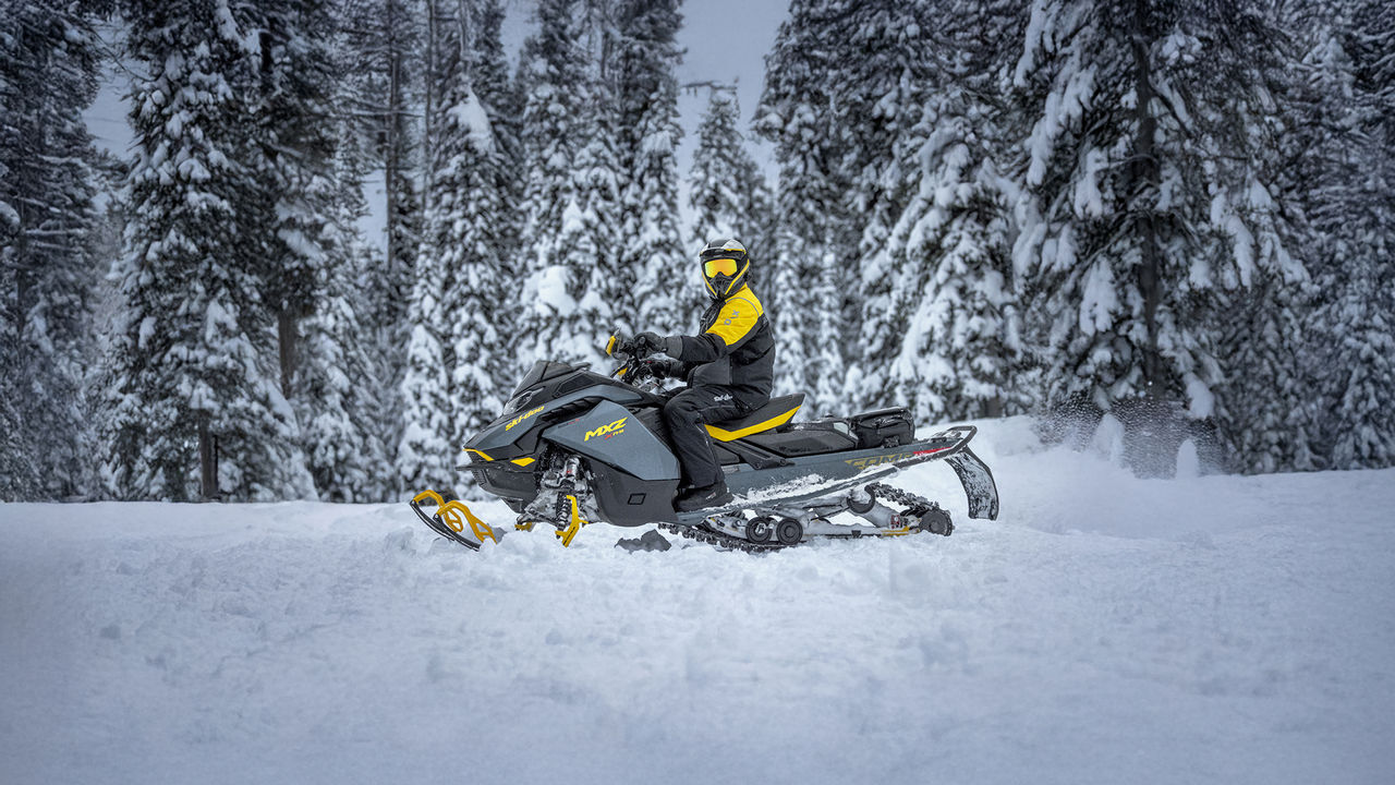 Rider wearing Ski-Doo branded snowmobiling gear on a MXZ snowmobile